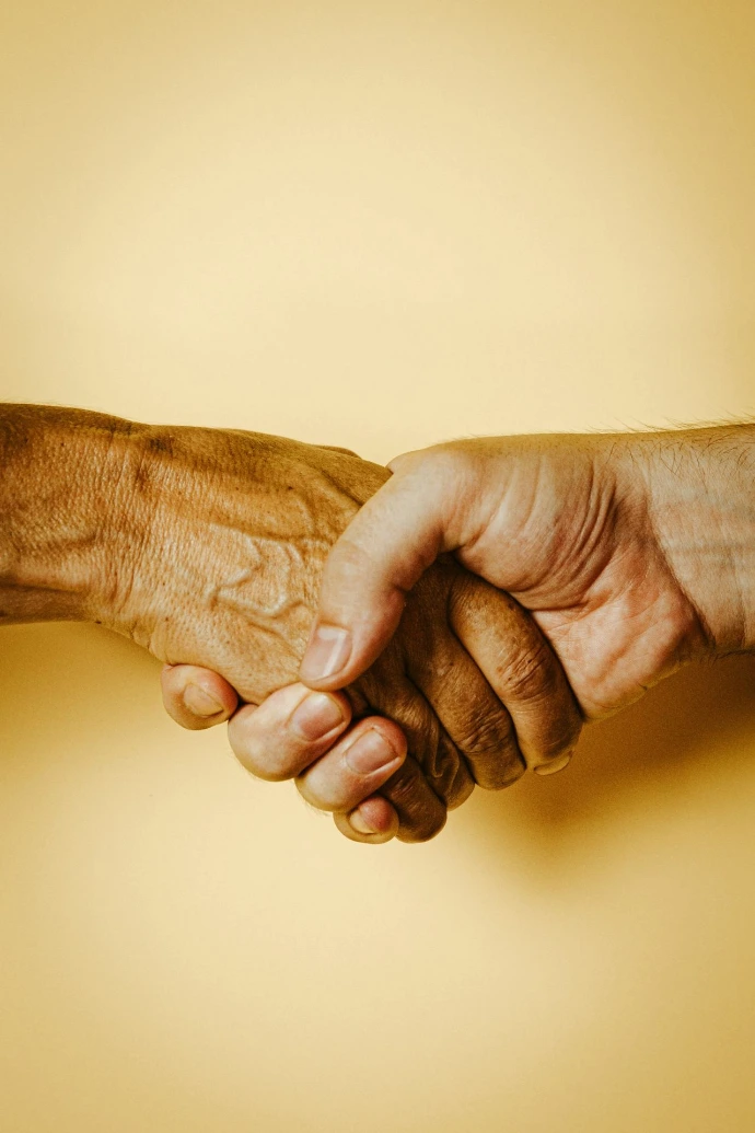 Two hands shaking against a plain light yellow background